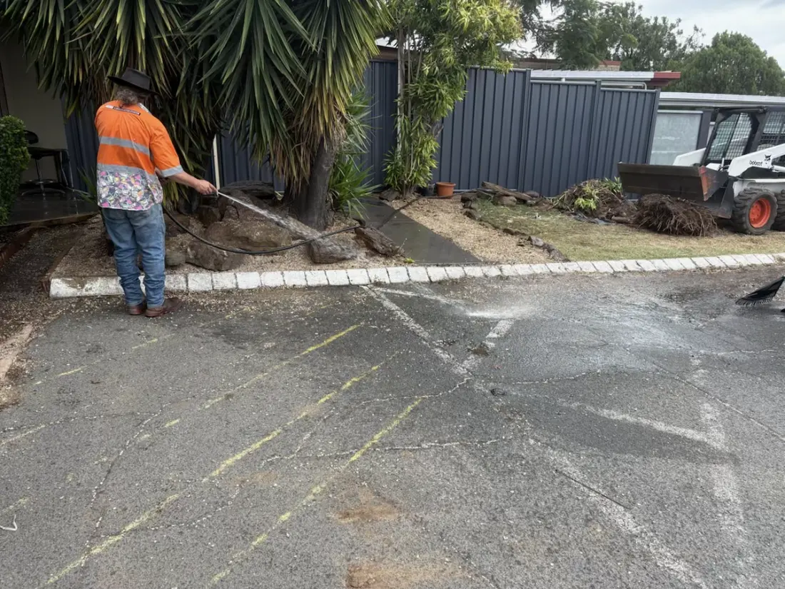 Operator washing down a carpark with a Bobcat nearby